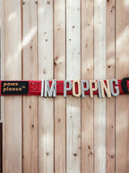 Red Pawz Please collar with charms spelling IM POPPING letters on a wooden background